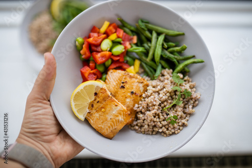 Hand holding salmon and buckwheat dish with green beans