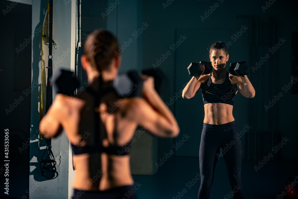 A young female doing exercise with a two dumbbell in front of a mirror A young female doing exercise with a two dumbbell in front of a mirror