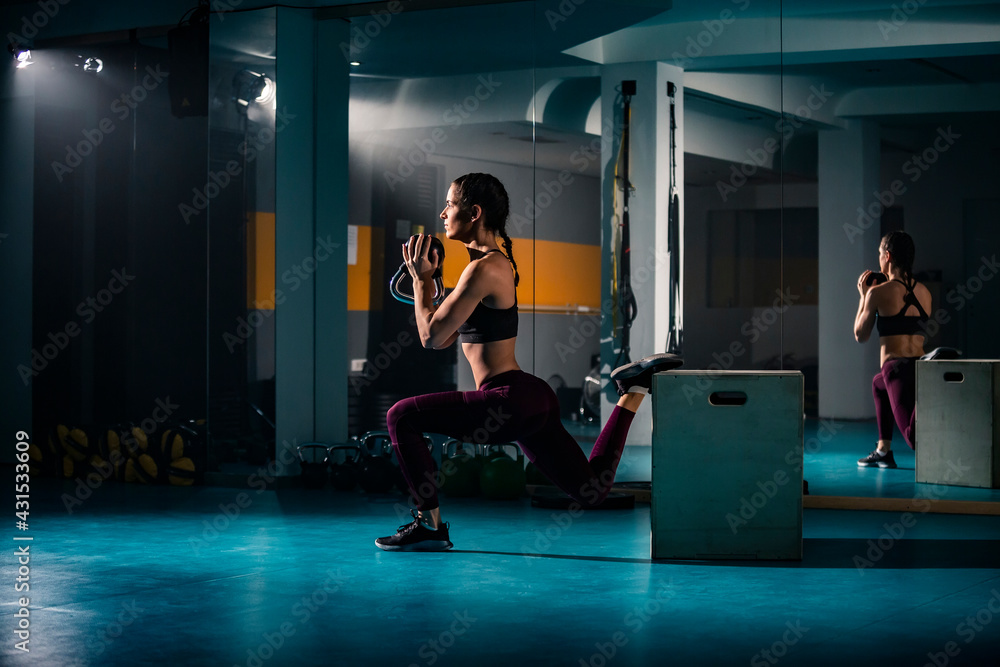 Fototapeta premium A young fit woman doing split squats exercise in gym