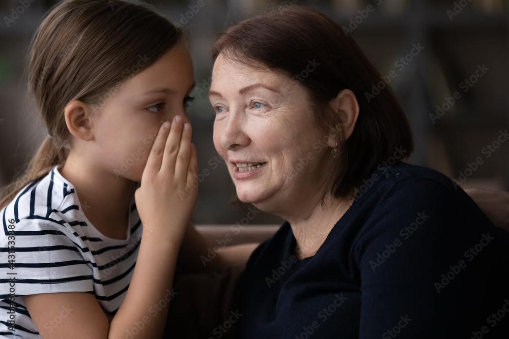 Small teenage girl child whisper in grandmother ear share secret with grandparent at home. Cute little teen granddaughter and elderly granny have fun talking gossiping together. Bonding concept. Small teenage girl child whisper in grandmother ear share secret with grandparent at home. Cute little teen granddaughter and elderly granny have fun talking gossiping together. Bonding concept.