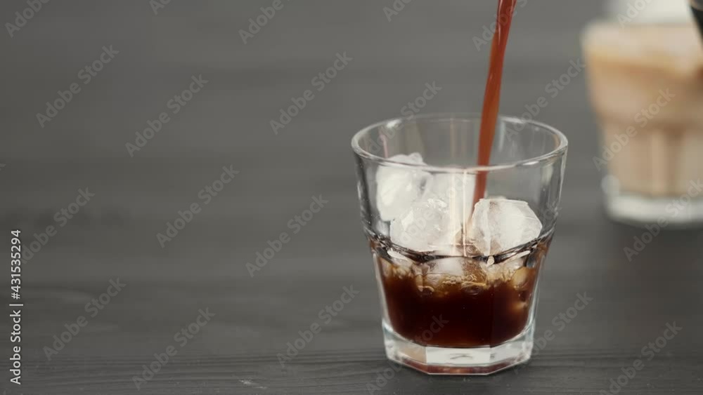 Preparing summer coffee drink with ice and milk. Ice is poured into glass and coffee is poured from coffee pot, selective focus. Close-up with copy space, concept of making drink in bar Preparing summer coffee drink with ice and milk. Ice is poured into glass and coffee is poured from coffee pot, selective focus. Close-up with copy space, concept of making drink in bar