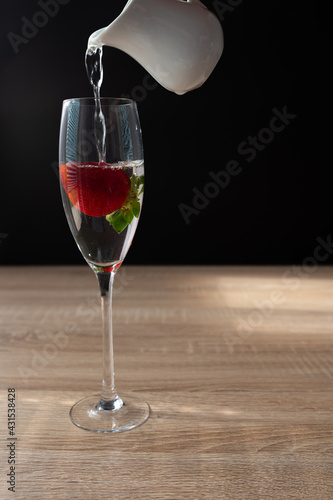 Ripe red strawberry in a glass of water. Splash in water on black background. Copy space