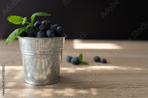 Fresh and sweet blueberry with mint in metal bucket on wooden table. Copy space.