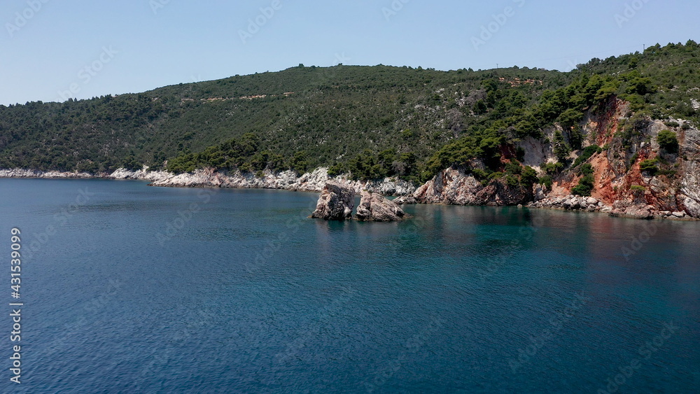 Naklejka premium Aerial drone views over a rocky coastline, crystal clear Aegean sea waters, touristic beaches and lots of greenery in Skopelos island, Greece. A typical view of many similar Greek islands.