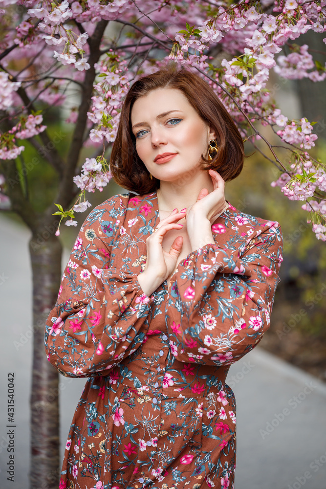 A woman walks along a spring street. The girl enjoys the scent of a blossoming tree. Beautiful woman in a dress with blooming cherry sakura A woman walks along a spring street. The girl enjoys the scent of a blossoming tree. Beautiful woman in a dress with blooming cherry sakura