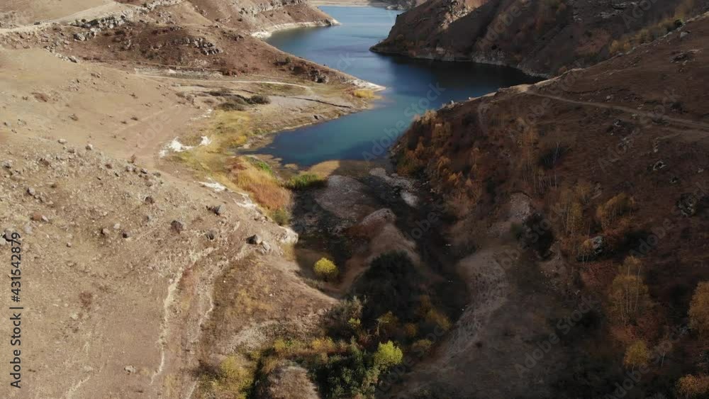 Aerial view of flight over a high mountain lake surrounded by rocks and hills on a sunny day Aerial view of flight over a high mountain lake surrounded by rocks and hills on a sunny day
