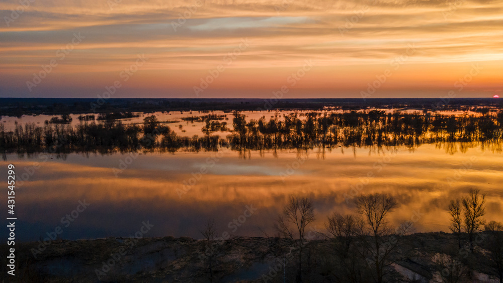 Aerial view of the setting sun beautifully illuminates cumulus clouds slowly floating over a full-flowing river on a warm spring evening. Sunset panorama over the river. Travel and journey concept. Aerial view of the setting sun beautifully illuminates cumulus clouds slowly floating over a full-flowing river on a warm spring evening. Sunset panorama over the river. Travel and journey concept.