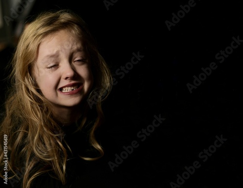 Horizontal, Close up portret of  crying young girl, on black background.