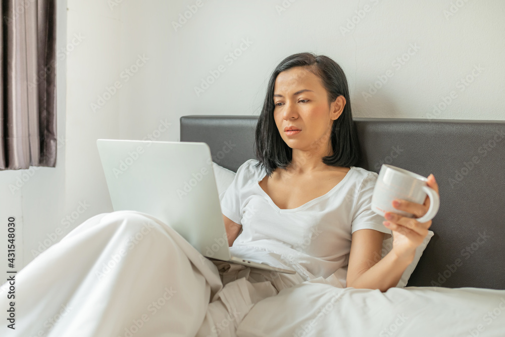 Happy casual beautiful woman working on a laptop sitting on the bed in the house. Coronavirus. Quarantine. Woman look at a laptop computer. Freelancer, distant work, work at home, online education. Happy casual beautiful woman working on a laptop sitting on the bed in the house. Coronavirus. Quarantine. Woman look at a laptop computer. Freelancer, distant work, work at home, online education.