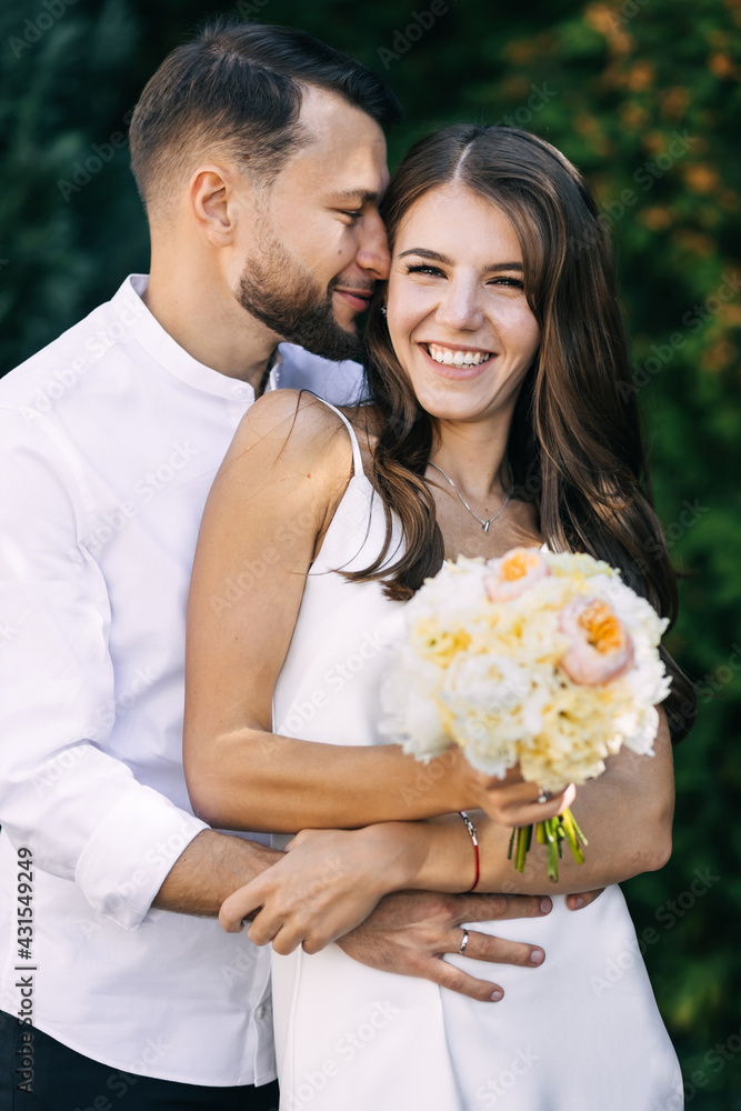 Sensual embrace of the bride and groom against the backdrop of greenery. relationships, family, wedding. Girl holding a beautiful bouquet with peony. Sensual embrace of the bride and groom against the backdrop of greenery. relationships, family, wedding. Girl holding a beautiful bouquet with peony.