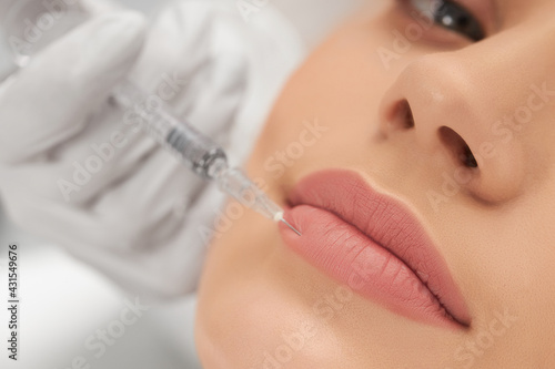 Close up of young attractive woman lying on procedure for lip augmentation in beautician. Concept of beauty procedure with good mood and with professional cosmetics.