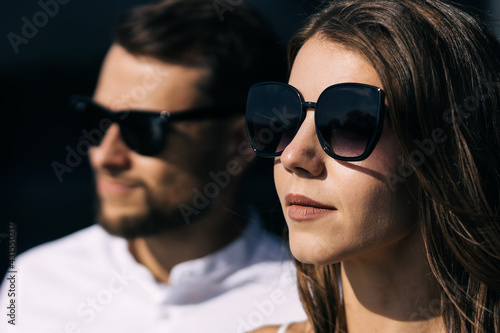 Close-up portrait of serious newlywed couple wearing black sunglasses looking into the distance.