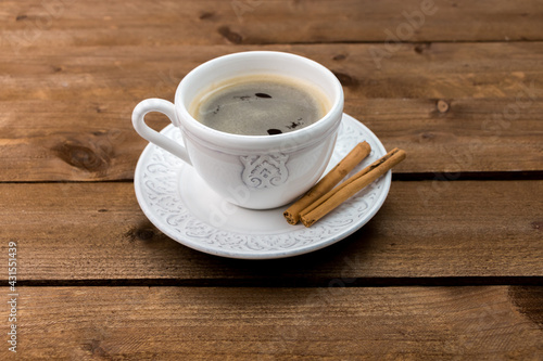 White vintage cup with coffee, espresso with cinnamon sticks on wooden table