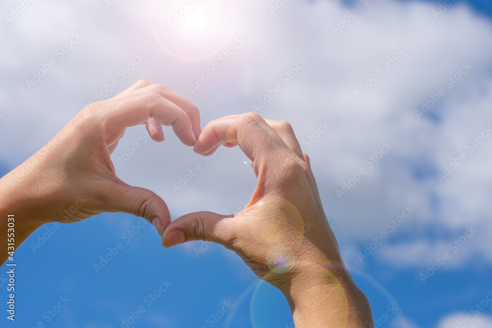Female young hands in heart shaped gesture on blue cloudy sky background and bright sunlight. Concept of love sicking, relationship, calmness and tranquility. Summer love mood Female young hands in heart shaped gesture on blue cloudy sky background and bright sunlight. Concept of love sicking, relationship, calmness and tranquility. Summer love mood