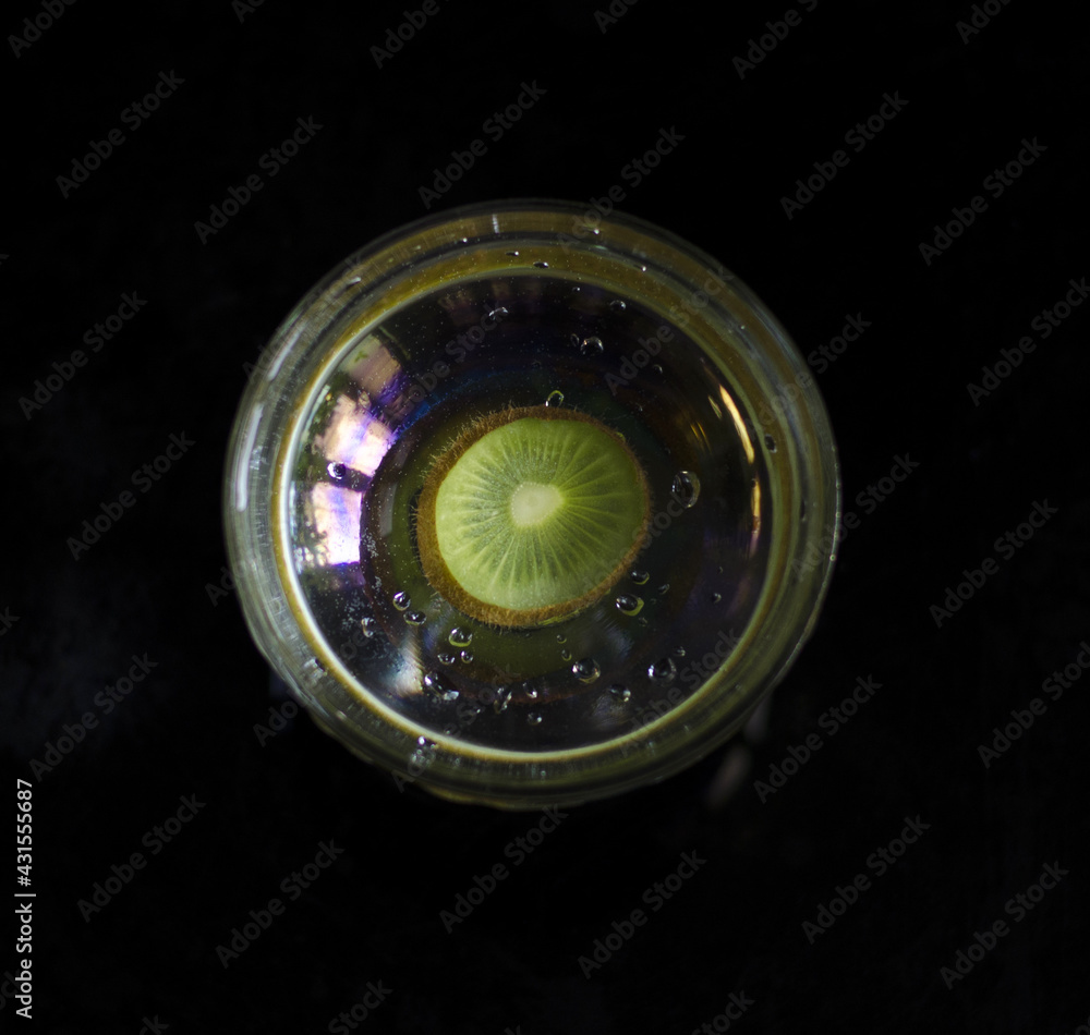 Top view. Round vase with water on black background, inside round slice of green kiwi. Design.