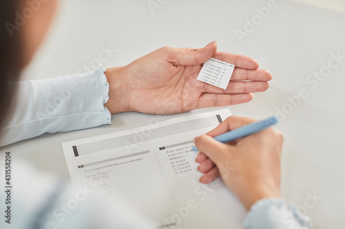 Fotografija High angle closeup of unrecognizable student holding cheat note while taking exa