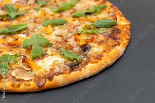 Closeup of a round pizza with cheese, chicken, mushrooms and arugula and spinach on a gray background.