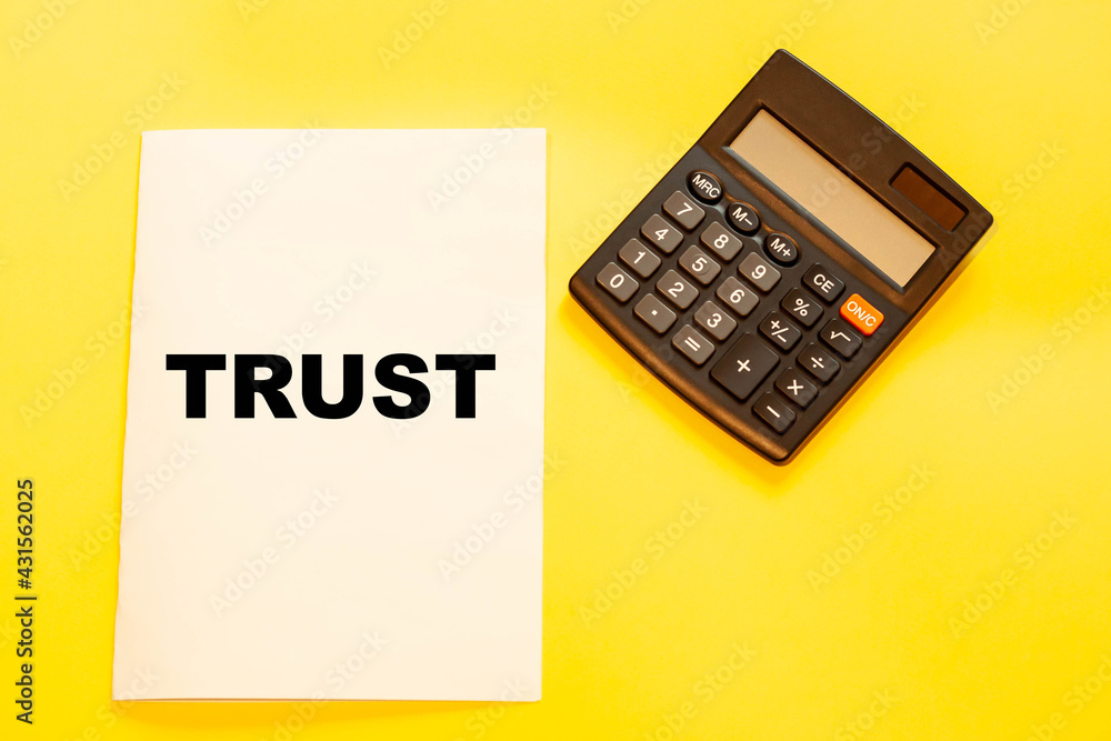 Business and financial text - TRUST, on white office paper next to a calculator Business and financial text - TRUST, on white office paper next to a calculator