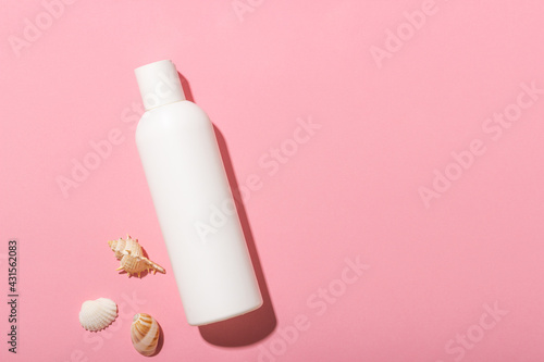 White cosmetic bottle with face cream or lotion and telana against a pink background with seashells. Sun cream, summer cosmetics.