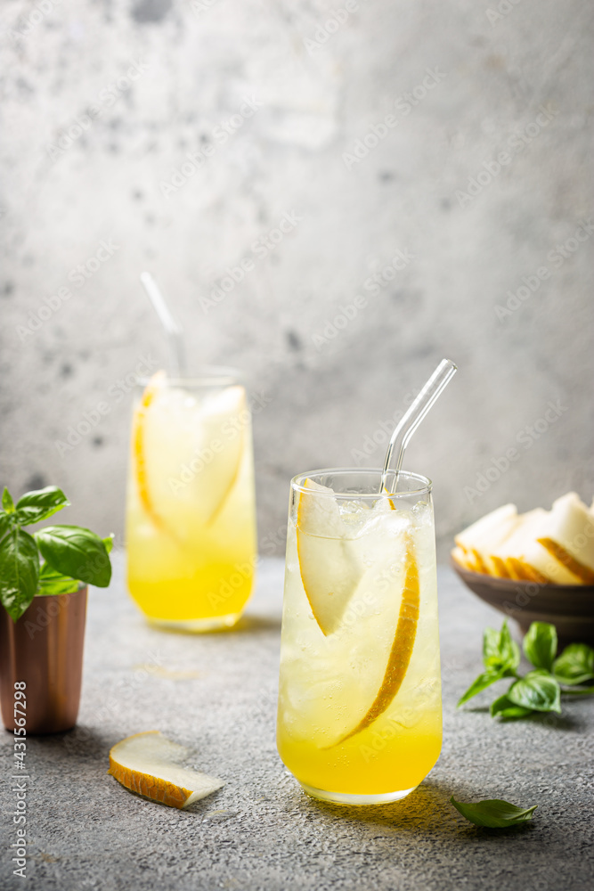 Fototapeta premium Melon juice, lemonade in glasses with ice and melon slices garnished with basil leaves. Concept of fresh summer drink