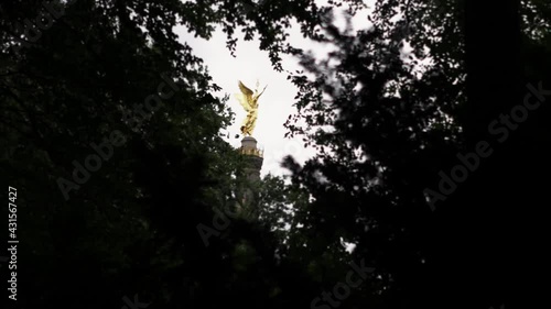 Golden statue among tree branches with sky in the background.
