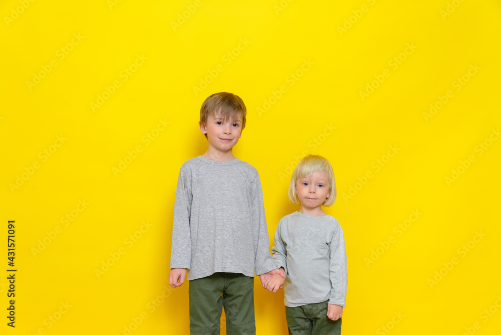 Portrait of two boys brothers smiling and holding hands. Studio photography on a yellow background, colored background. Portrait of two boys brothers smiling and holding hands. Studio photography on a yellow background, colored background.