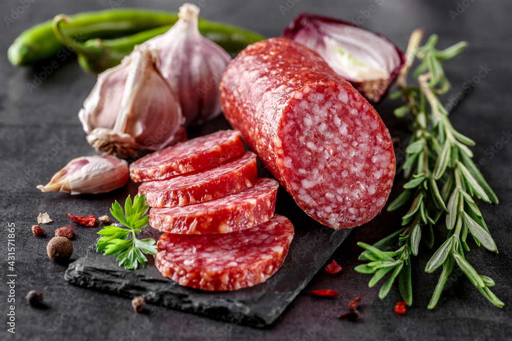 Traditional smoked salami sausage with spices.Salami sausage slices on a black chopping Board. Dark background. - obrazy, fototapety, plakaty 