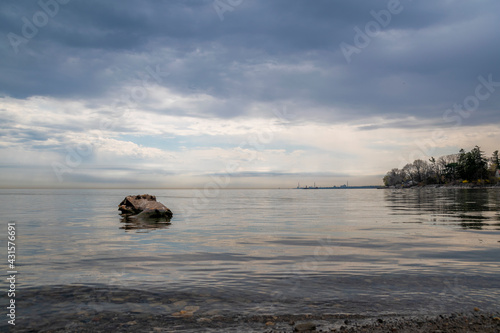 A log rests close to the shore of Lake Ontario in R.K. McMillan Park in Mississauga, against the backdrop of a dramatic sky on a damp and cloudy early-Spring day.