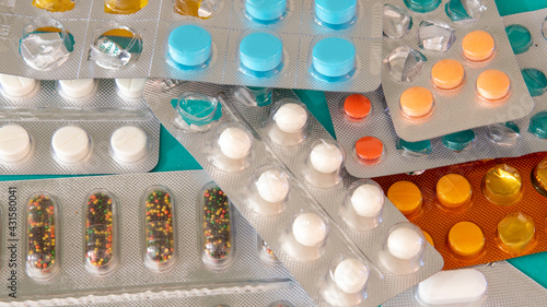 Flat lay view of a bunch of colorful pills in their blister. On top of a cyan wooden surface