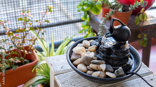 Close view of a decorative zen water fountain next to a few green plants on a warm spring afternoon