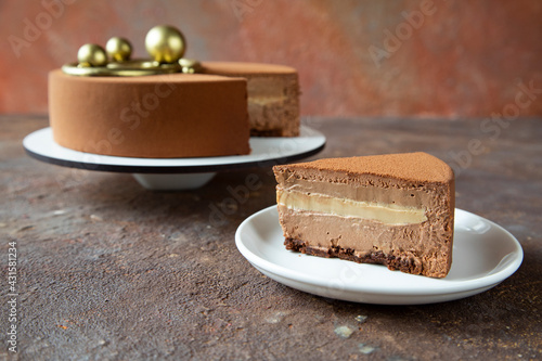 A piece of chocolate mousse cake on the background of a large cake decorated with golden spheres - the concept of a festive dessert for a birthday or Christmas