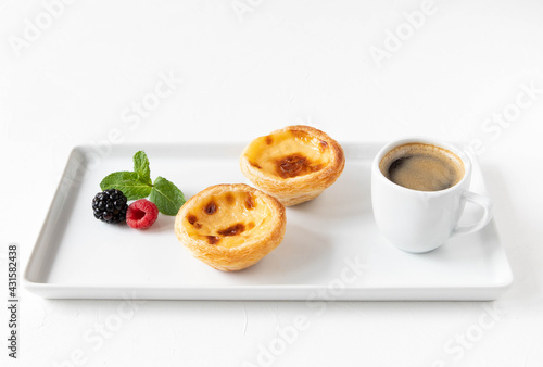 Breakfast with pastries from Portugal Pastel de nata cake, hot coffee and fresh berries - blackberries, raspberries with a mint leaf on a large white plate - romantic concept of the morning