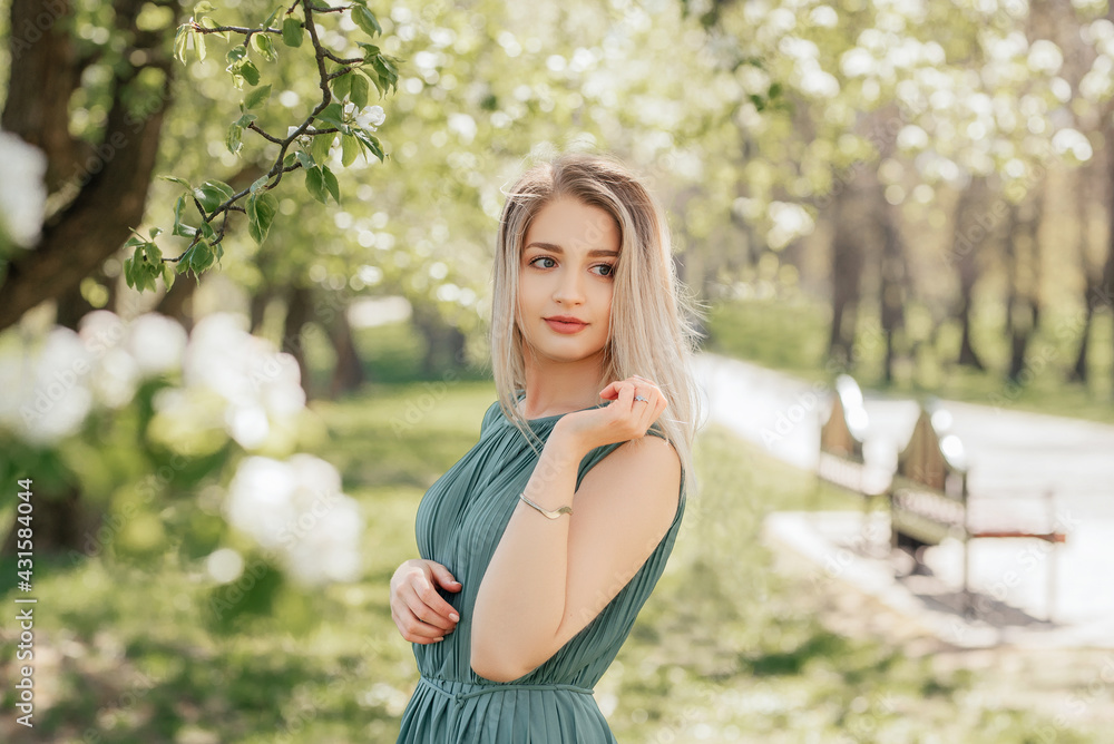 Beautiful young blonde woman in green dress in spring flowers garden. Woman outdoor. Beautiful young blonde woman in green dress in spring flowers garden. Woman outdoor.