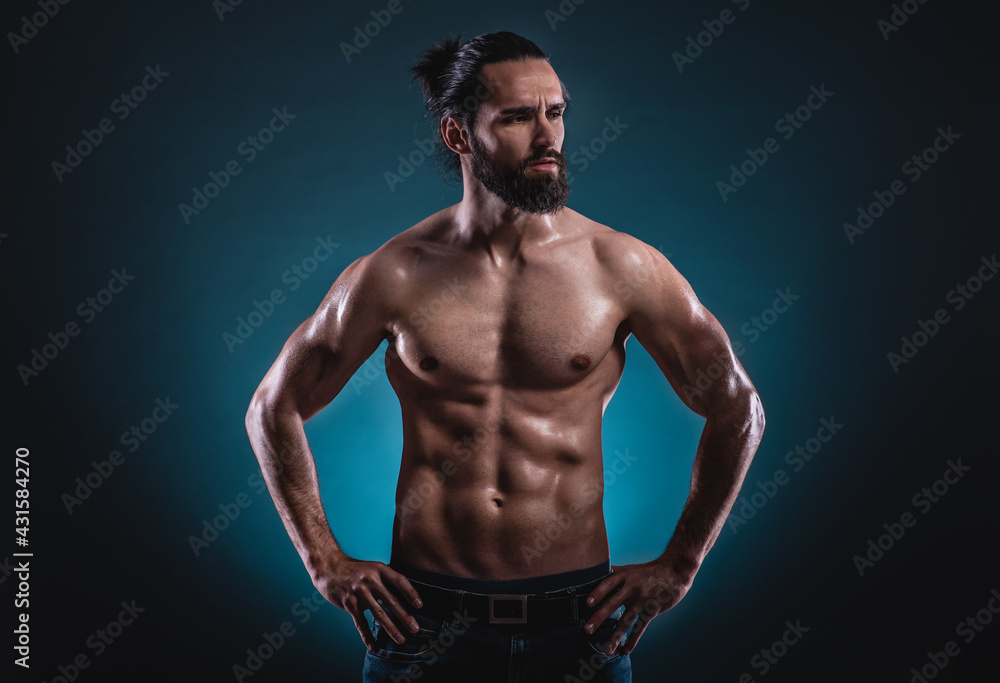 Studio portrait of a beautiful masculine bearded shirtless man showing his abdomen muscles