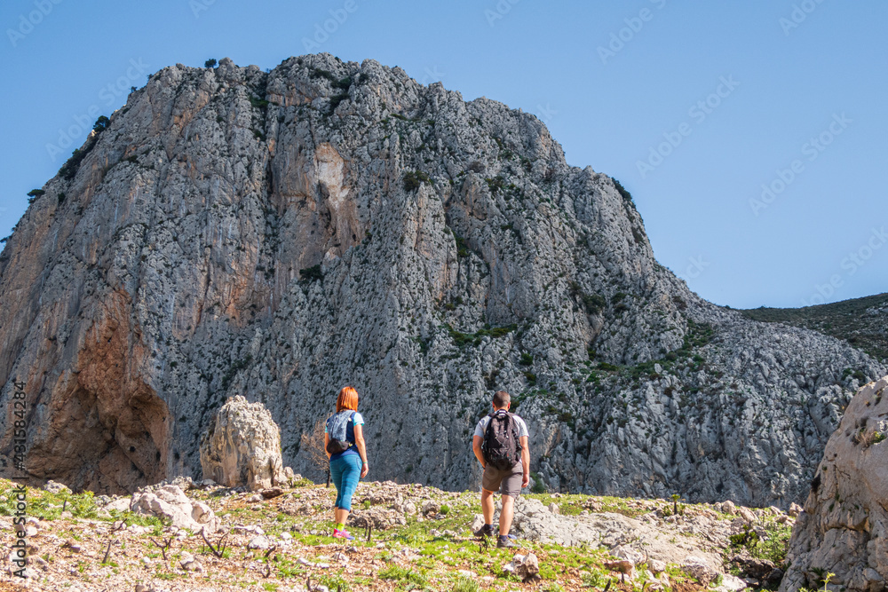 Hikers climbing a stony path up the side of a mountain on a sunny day.