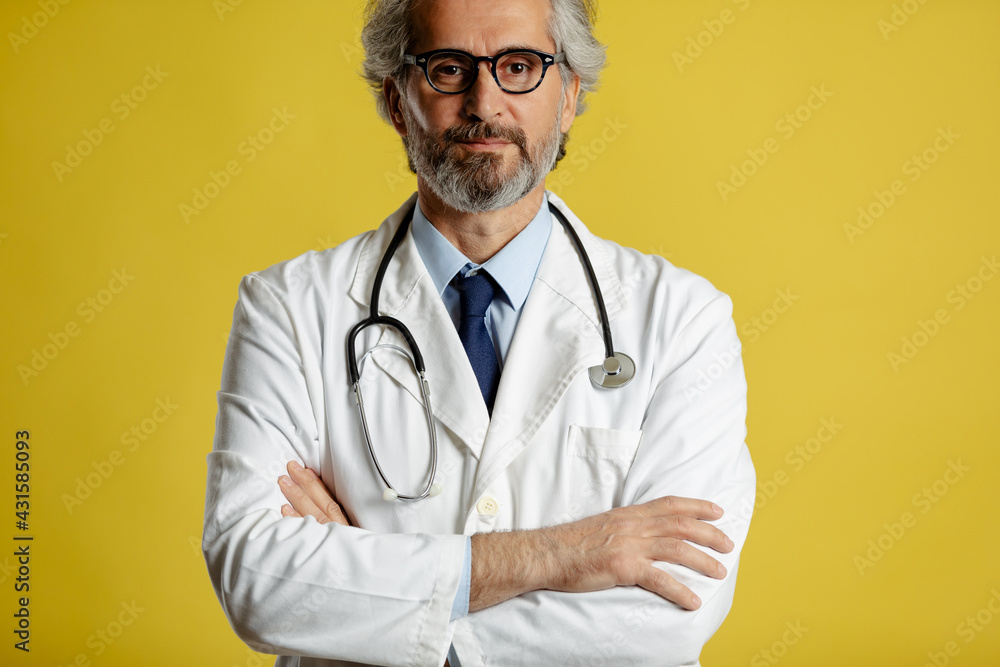 Portrait of senior doctor with eyeglasses and stethoscope standing and posing on yellow background. Portrait of senior doctor with eyeglasses and stethoscope standing and posing on yellow background.