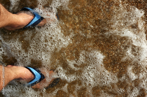 male feet in beach slippers ankle-deep in transparent sea water
