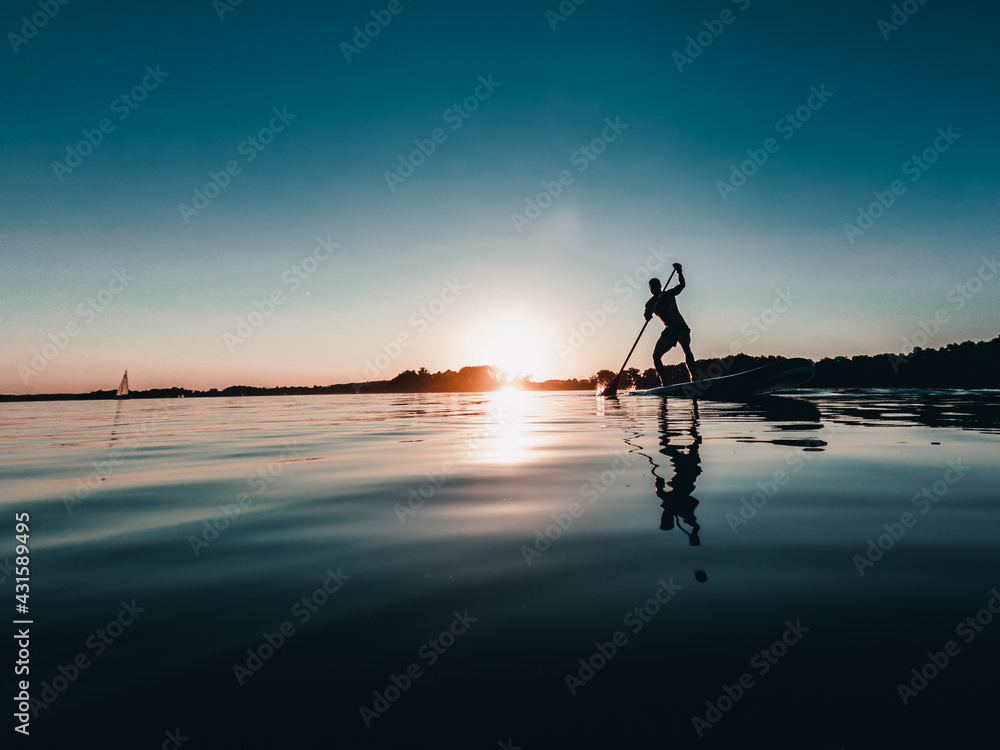 Mężczyzna na desce SUP o zachodzie słońca nad jeziorem