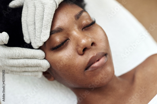 A dark-skinned model lies on the couch at the beautician and receives a microcurrent massage. Microcurrent therapy