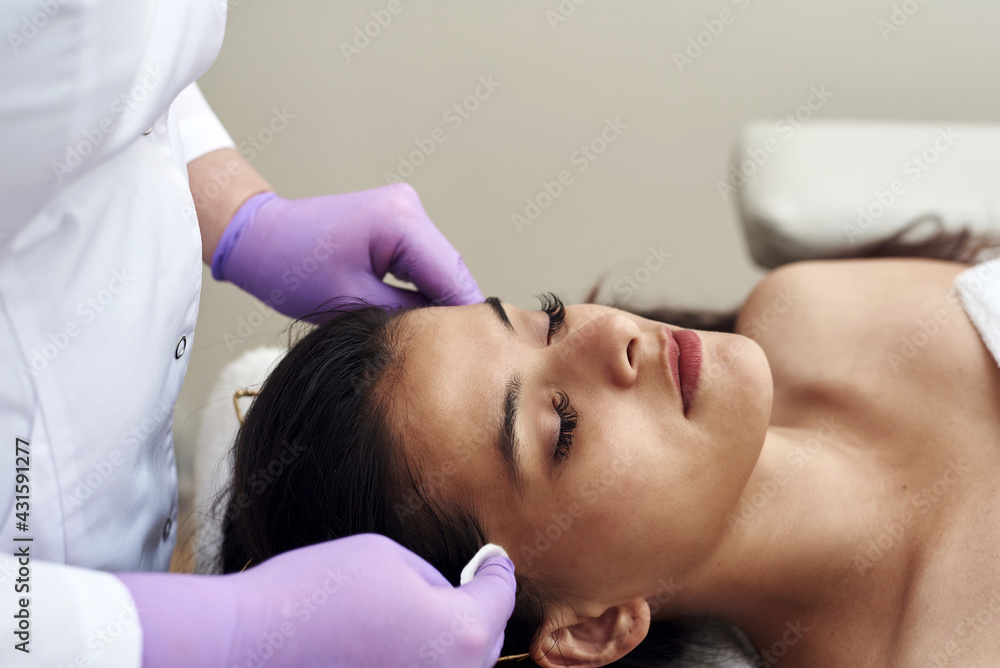 Young beautiful dark-haired woman lies in the beautician's office and makes face peeling. Cleansing the skin with cotton pads Young beautiful dark-haired woman lies in the beautician's office and makes face peeling. Cleansing the skin with cotton pads