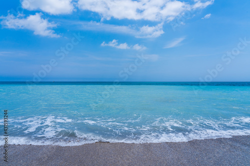 Turquoise sea, gray sand, blue sky. A small ship in the distance on the horizon