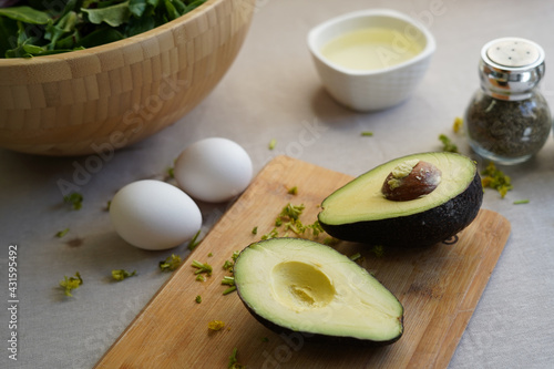 Two part of avocado with spices, eggs, avocado oil and salad on a wooden board on a light background 