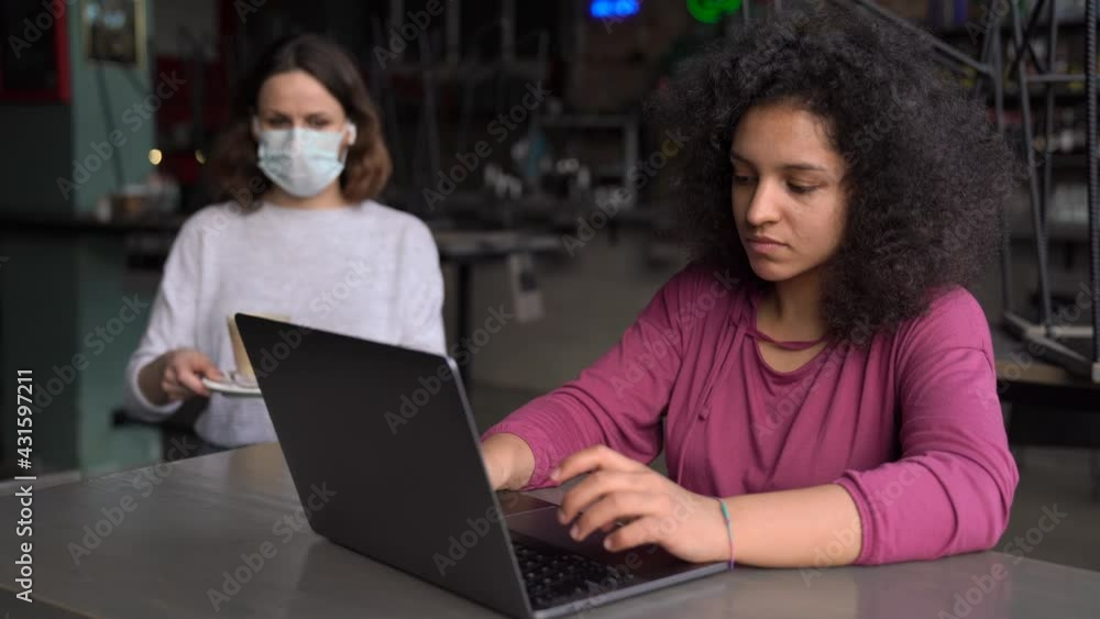 A Stressed African American Woman Working in The Morning From Caffe. The Waiters in Mask Bring a Coffee A Stressed African American Woman Working in The Morning From Caffe. The Waiters in Mask Bring a Coffee