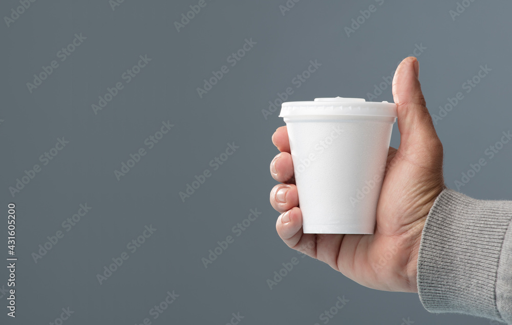 white thermal glass with lid in hand, gray background white thermal glass with lid in hand, gray background