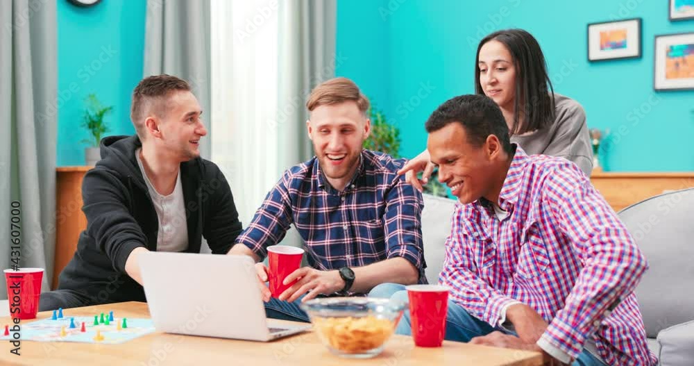 Happy diverse friends watching funny video, laughing at joke, using laptop, having fun together, sitting on couch, looking at computer screen, students colleagues working on online project Happy diverse friends watching funny video, laughing at joke, using laptop, having fun together, sitting on couch, looking at computer screen, students colleagues working on online project