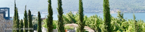 Panorama picture of scenery view in the sunny day. Beautiful blue sky, islands, green mountain, boats and fresh ocean on the beach. Cypress in the foreground. Summer vacation concept.