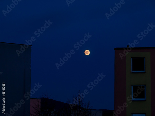 Super full moon between houses in the dark blue sky - April 2021
