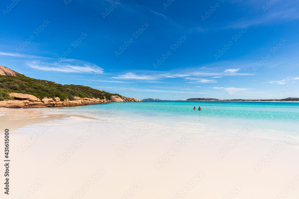 A young couple swim in the sparkling water next to the pristine white sand beach of Wharton Bay in the Cape LeGrande National Park on a clear summer day.