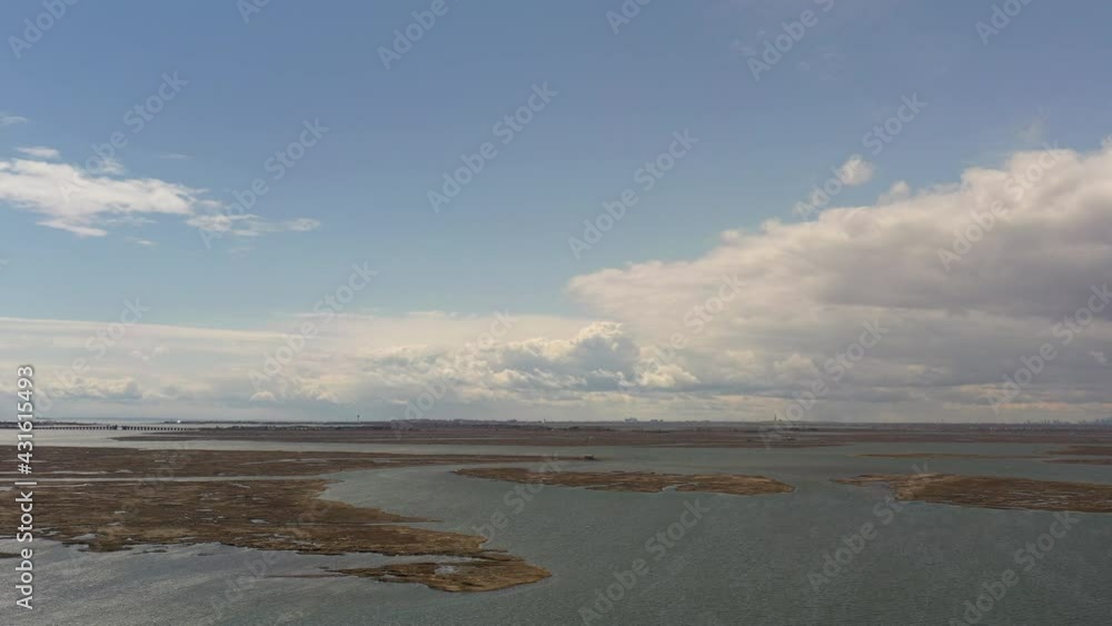 An aerial view on a beautiful day near a bay. The drone camera boom down with the waters, marsh with a cloudy, blue sky in the background.