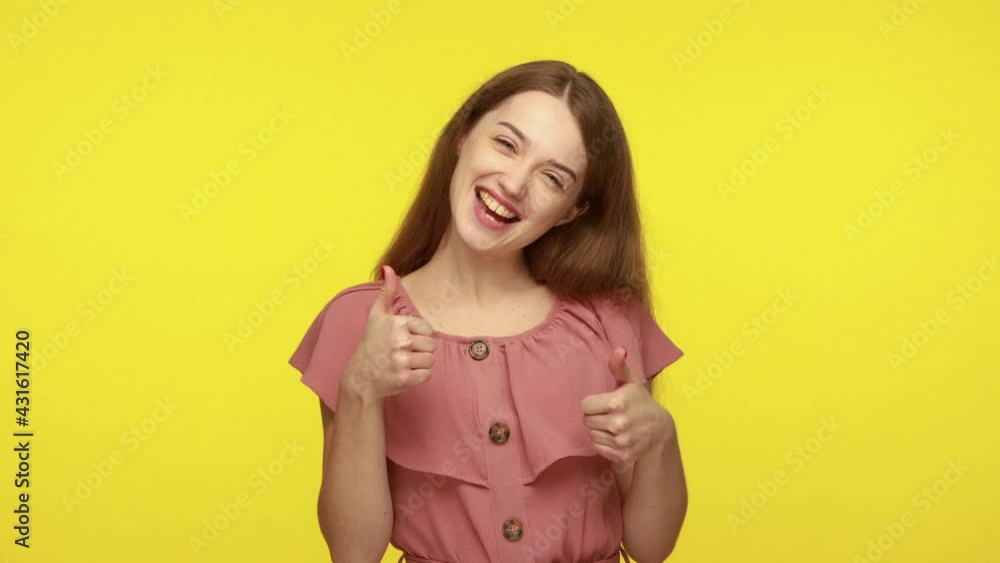 Cheerful beautiful young woman makes thumb up gesture approves your suggestion, gives recommendation, smiles broadly dressed in elegant dress. Indoor studio shot isolated on yellow background. Cheerful beautiful young woman makes thumb up gesture approves your suggestion, gives recommendation, smiles broadly dressed in elegant dress. Indoor studio shot isolated on yellow background.